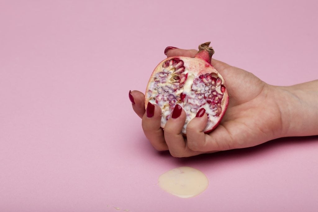 Rich pomegranate half in hand on pink background, healthy fruit, antioxidant-rich, fresh pomegranate, fruit nutrition, natural superfood, vibrant red seeds, pink backdrop, healthy lifestyle, organic produce.