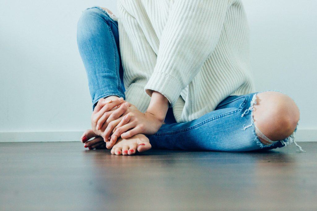 Relaxed woman sitting cross-legged on the floor, wearing ripped jeans and a cozy sweater, embodying comfort and mindfulness.