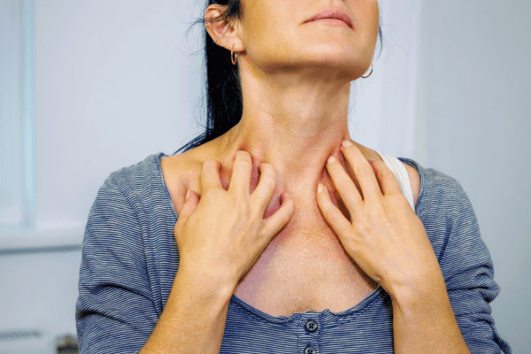 A woman experiencing throat discomfort, holding her neck with both hands, in a clinical setting, highlighting symptoms related to throat or thyroid issues, with a focus on health and medical care.